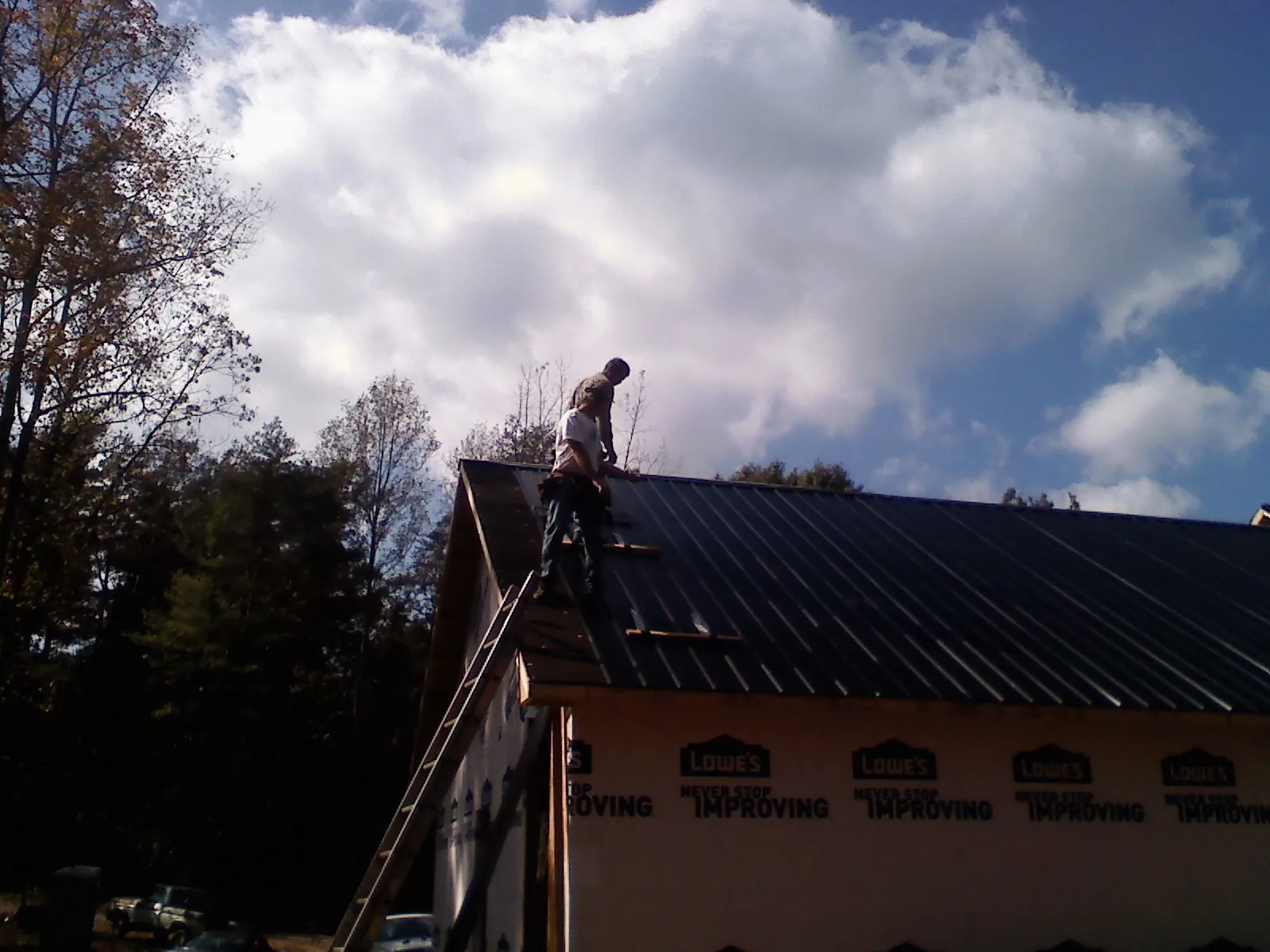 Roofer fastening dark metal panels high against a cloudy sky, from a Roof Inspection job in Elmsford