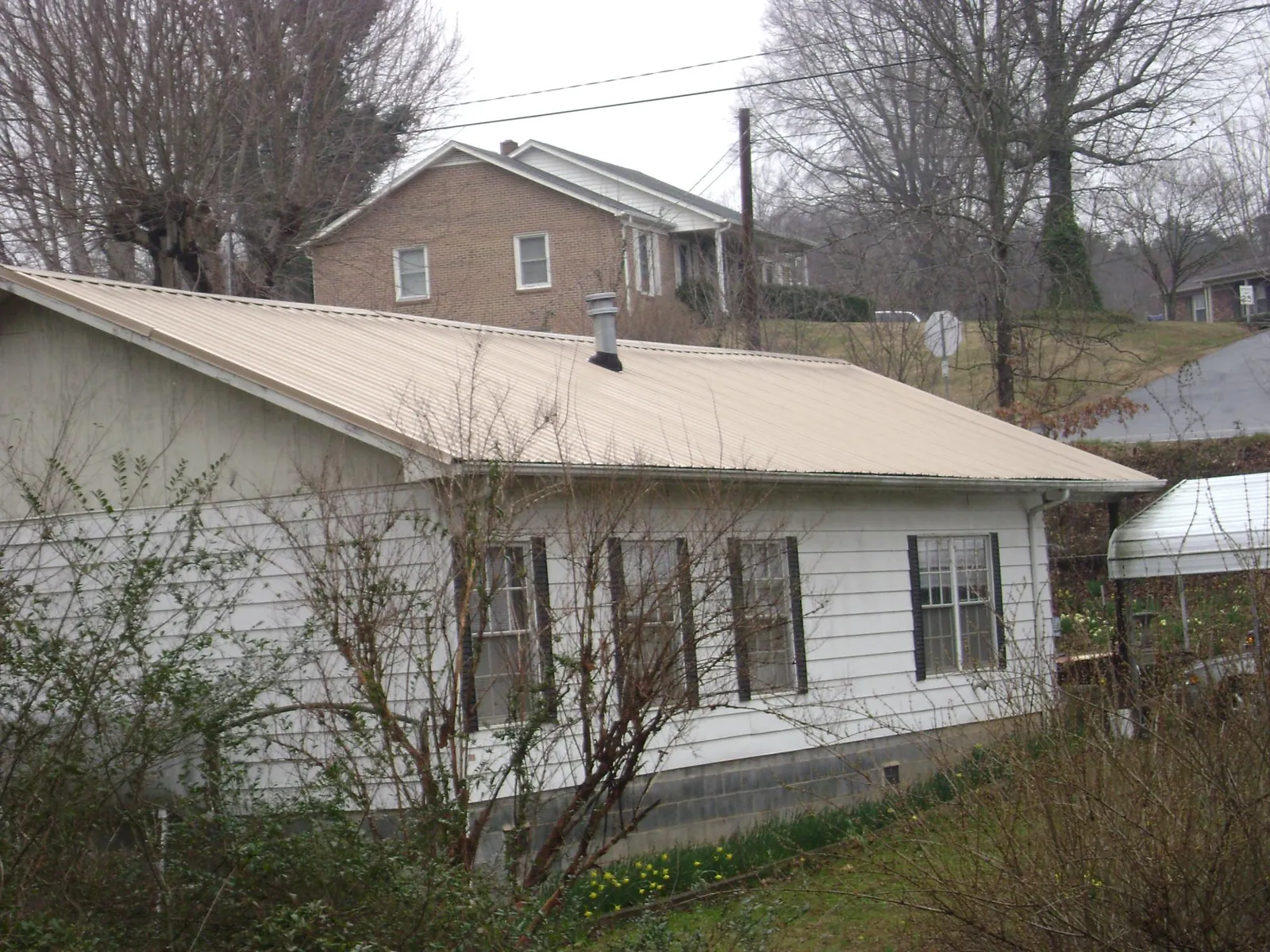 Tan metal roof on a white sided house set into a hillside — Commercial Roofing by Roofing Brothers in Elmsford