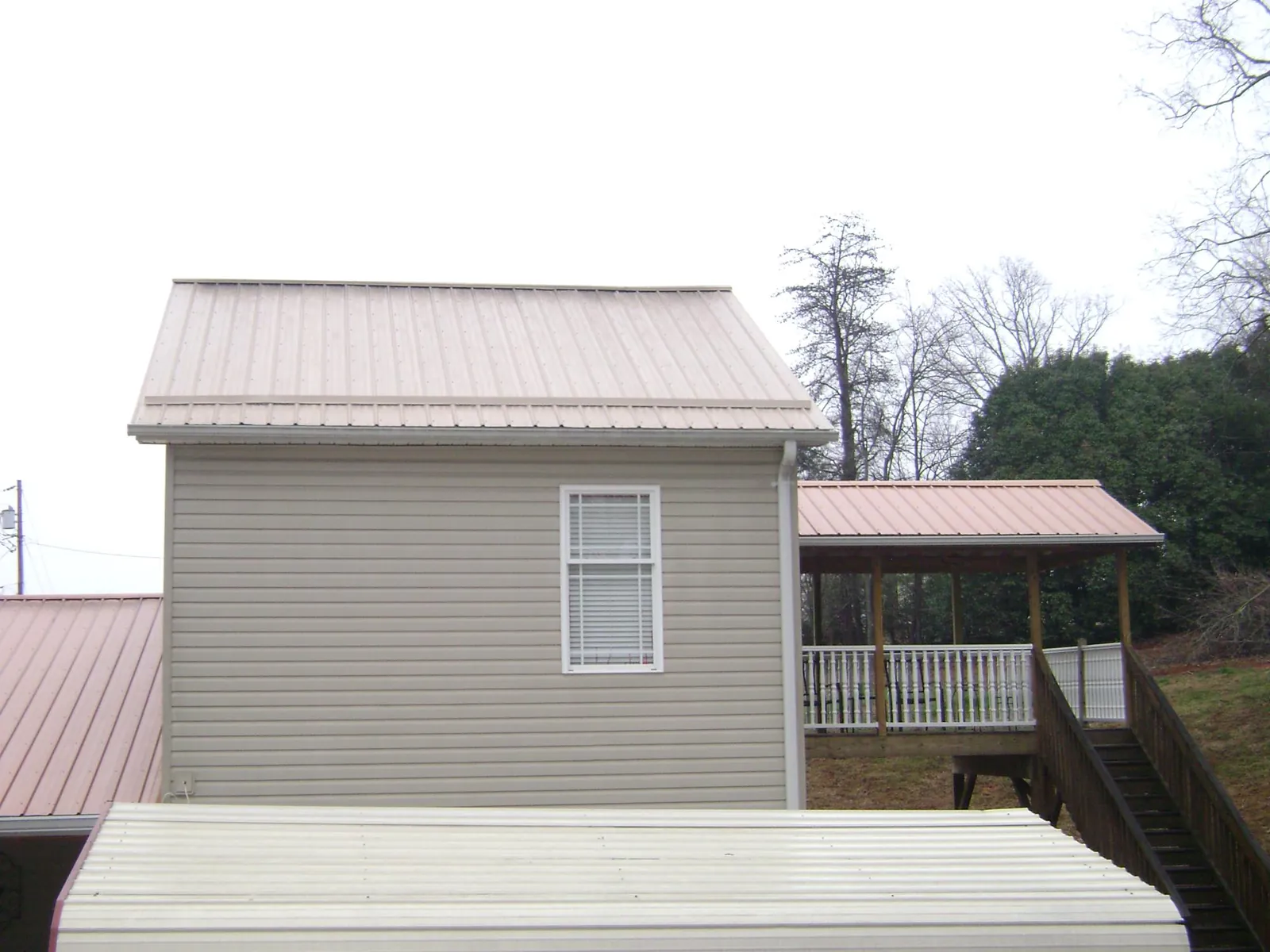Tan metal roofs on a two story addition and attached porch, from a Roof Replacement job in Elmsford