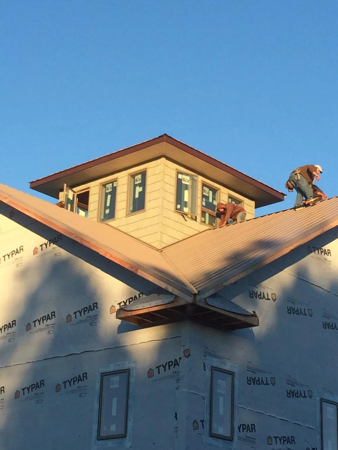 Roofers working around a rooftop cupola on a new metal roof at sunset — Roof Waterproofing in Elmsford by Roofing Brothers